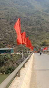 Bridge with Red Flags – Rider Crossing on Ha Giang Loop, North Vietnam Red flags on poles along a bridge with a solitary rider crossing on the Ha Giang Loop, North Vietnam