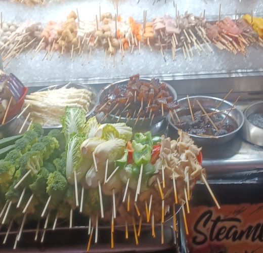 Pre-skewered kebabs with fresh vegetables in the foreground, and meat and seafood on ice at a stall in Chinatown, Kuala Lumpur