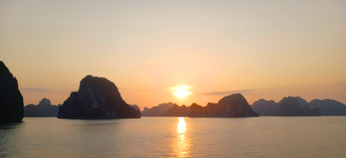 Sunset at Ha Long Bay, Vietnam, with sun setting between karsts and water in the foreground
