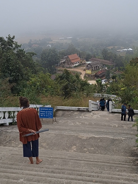 A pilgrim stands at the top of the stairs to the White Buddha in Pai, reflecting on the foggy village below in the early morning mist