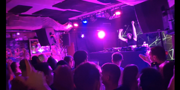 Crowd dancing with a DJ raising arms in the air and spectacular lighting effects at a ruin bar in Budapest
