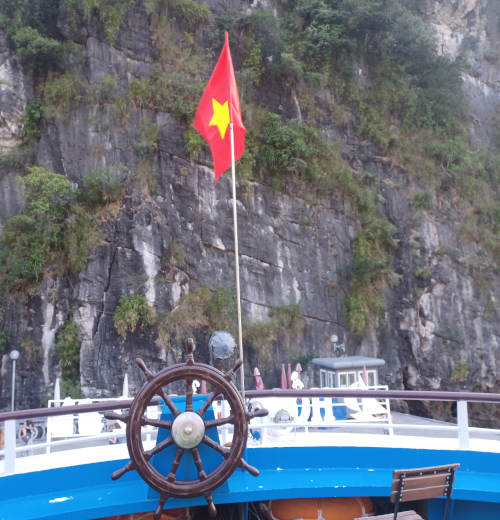 Front view of the boat with steering wheel and Vietnamese flag against a karst