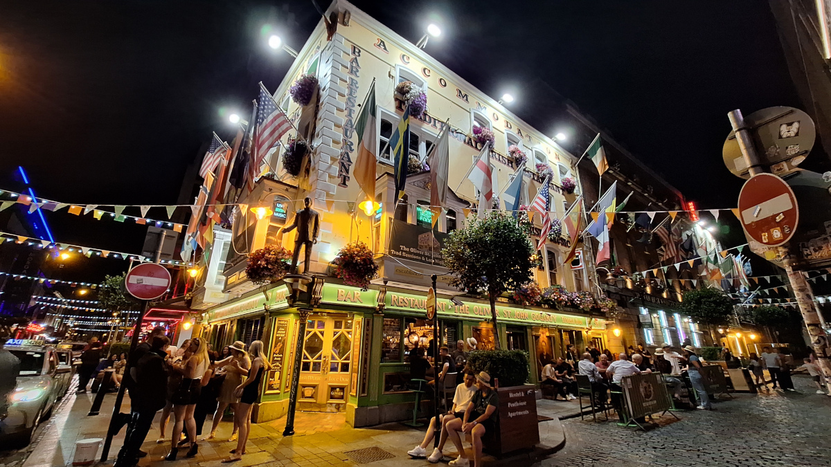 Pub in Temple Bar, Dublin on a Summer Evening Pub in Temple Bar area, Dublin, Ireland, adorned with flags and illuminated on a dark summer evening with people passing by