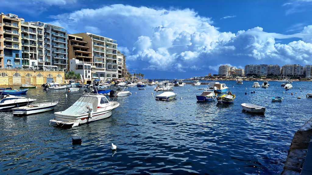 Charming Scene at Spinola Bay Spinola Bay featuring small fishing and recreational boats, with buildings on the left side and open sea occupying the rest of the image