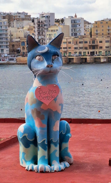 Whimsical Cat Installation Overlooking Spinola Bay Large blue cat installation on a rooftop with quirky green and brown patches, overlooking Spinola Bay and St. Julian's