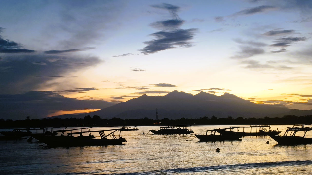 Stunning Sunrise over Mount Rinjani Sunrise over Mount Rinjani with shades of orange, red, and blue in the sky; boats silhouetted in the foreground