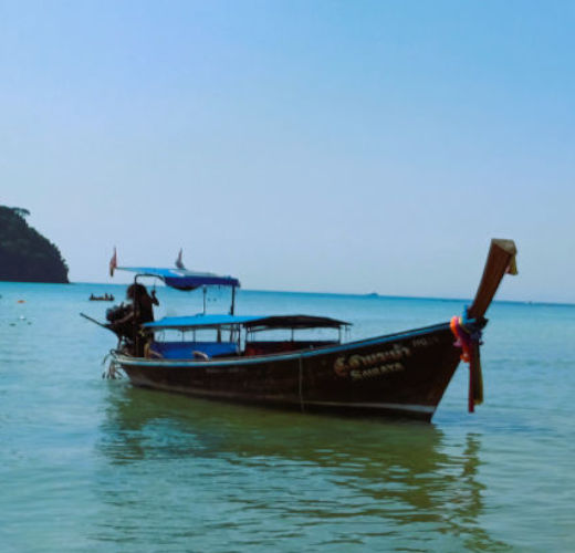 Empty long-tail boat moored in Tonsai Bay, surrounded by the calm waters of the Andaman Sea and a clear blue sky