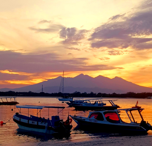 Boats docked in the sea at Gili Trawangan, Indonesia, with a stunning sunrise over Mount Rinjani in Lombok